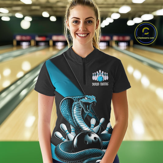 Female model at the bowling lane wearing a black quarter-zip decorated with blue cobra artwork and bowling graphics.