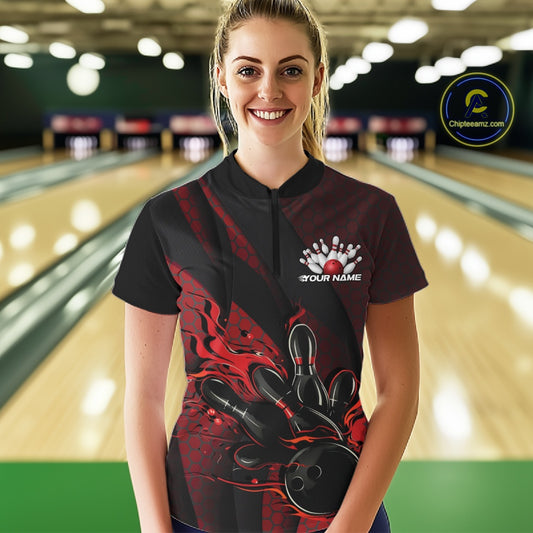 Female model in a bowling lane wearing a black and red quarter zip shirt, front view showcasing flames bowling ball hitting pins with geometric textures
