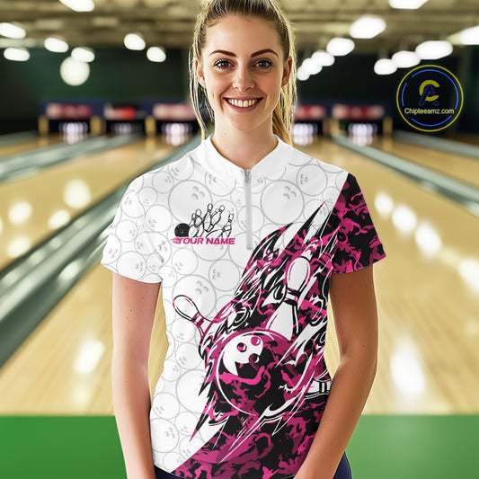 Female model wearing a white bowling quarter-zip shirt at the lane with pink camo-inspired bowling graphics and subtle bowling ball patterns.