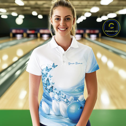 Female model wearing a white and blue bowling polo shirt with butterfly artwork and bowling-themed graphics at the bowling lane.