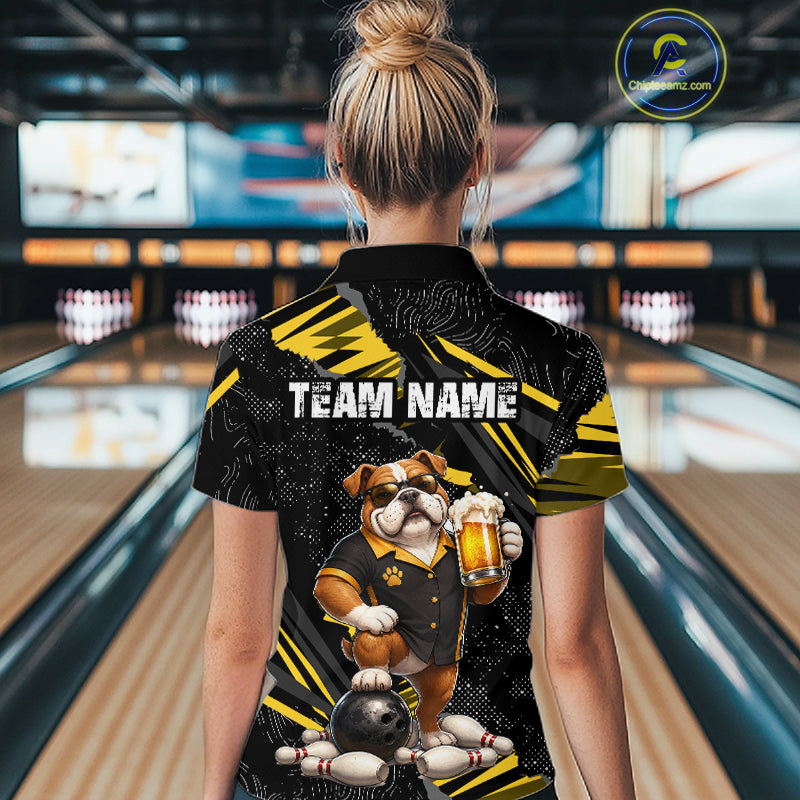 A woman viewed from behind wearing a black and yellow bowling-themed short-sleeve polo shirt with a bulldog graphic and 'TEAM NAME' text, standing in a bowling alley.