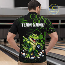 Load image into Gallery viewer, A man viewed from behind wearing a black short-sleeve bowling shirt with a green cartoon dinosaur graphic and the text 'TEAM NAME' on the back. Bowling lanes are visible in the background, and a 'Chipteeteamz'.