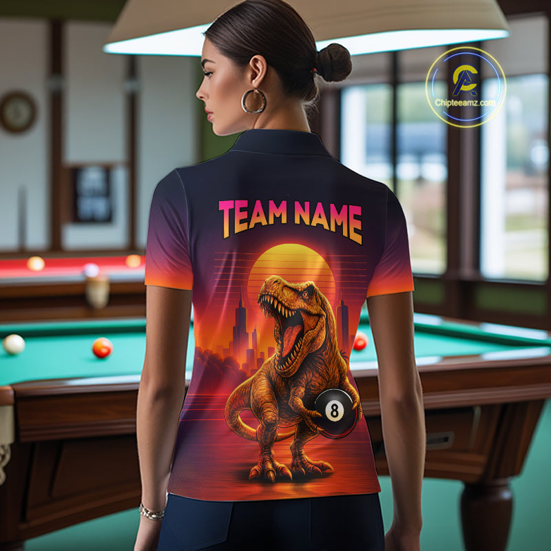 A woman stands in a billiards room wearing a short-sleeve collared shirt from the back, featuring a large graphic of a roaring T-rex holding an 8-ball under a sunset and the words 'TEAM NAME'.
