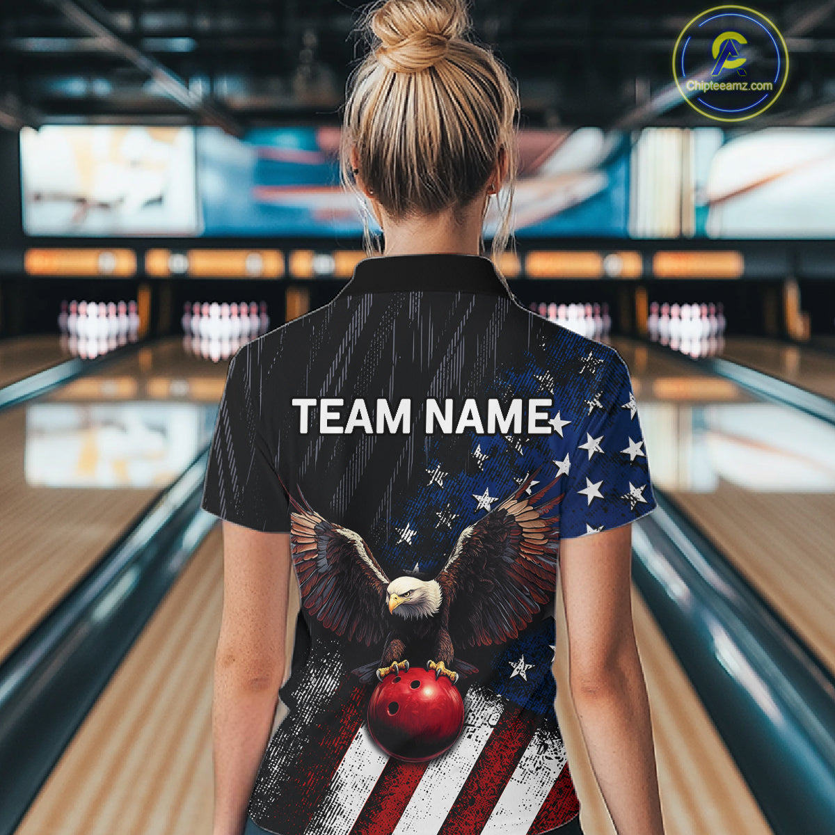 A woman viewed from behind wearing a custom bowling shirt with a patriotic American flag design featuring a bald eagle and bowling ball graphic, with 'TEAM NAME' printed on the back. The background shows a blurred bowling alley.