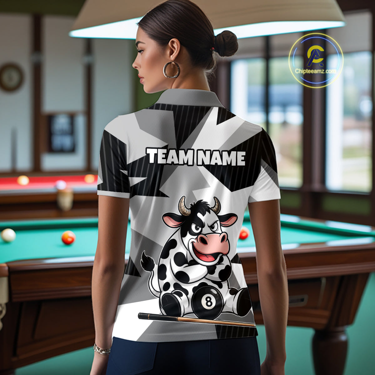 Person wearing a polo shirt with a cow design and 'Team Name' text in a pool hall.