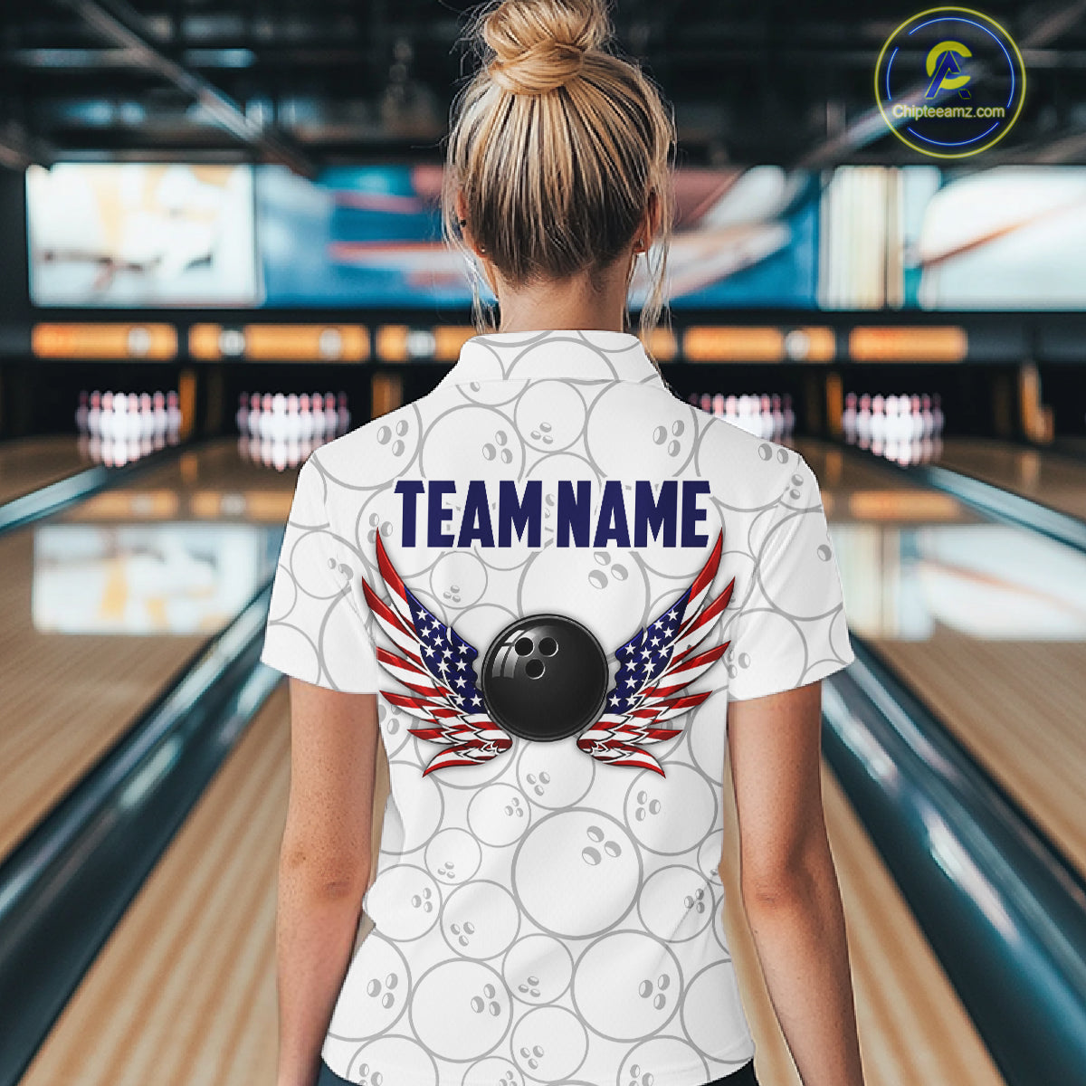 A woman viewed from behind wearing a white bowling-themed polo shirt with a pattern of bowling balls, a black bowling ball graphic, and wings with an American flag design. The shirt has 'TEAM NAME' printed on the back.