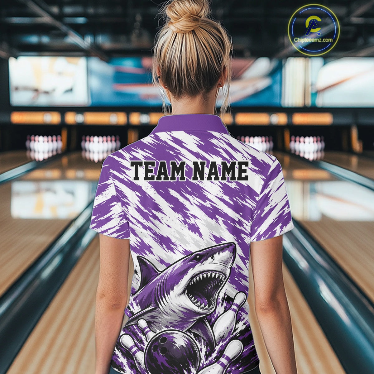 Person wearing a purple and white bowling shirt with a shark design and 'TEAM NAME' text in a bowling alley.