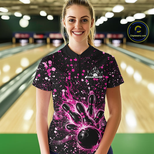 Female model wearing a black bowling quarter-zip shirt at the bowling lane with pink music-themed paint splatter bowling graphics.