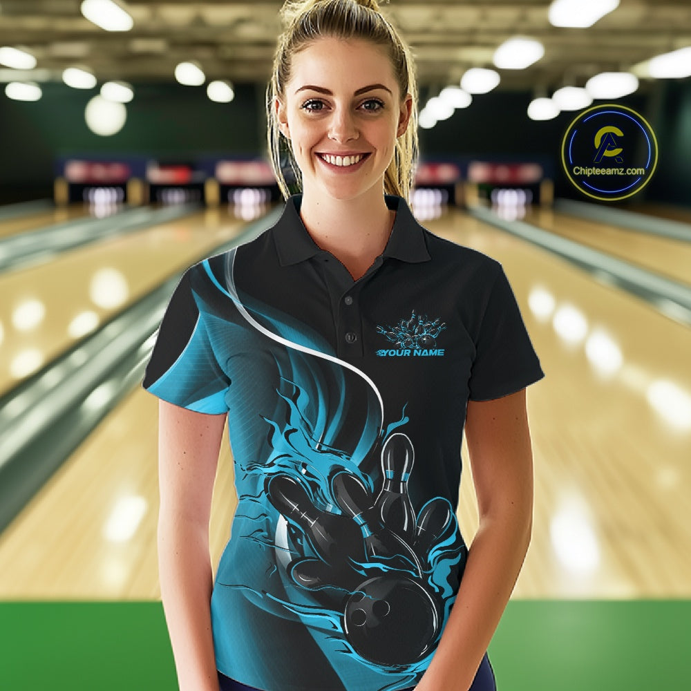 Female model front view in bowling venue wearing black and blue polo shirt with flaming bowling ball knocking down pins in energetic action scene.