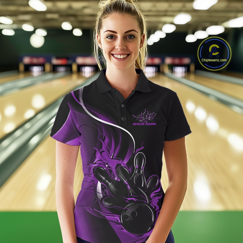 Female model front view in a bowling lane wearing a black and purple polo shirt featuring flame bowling ball striking pins in dynamic sports artwork.