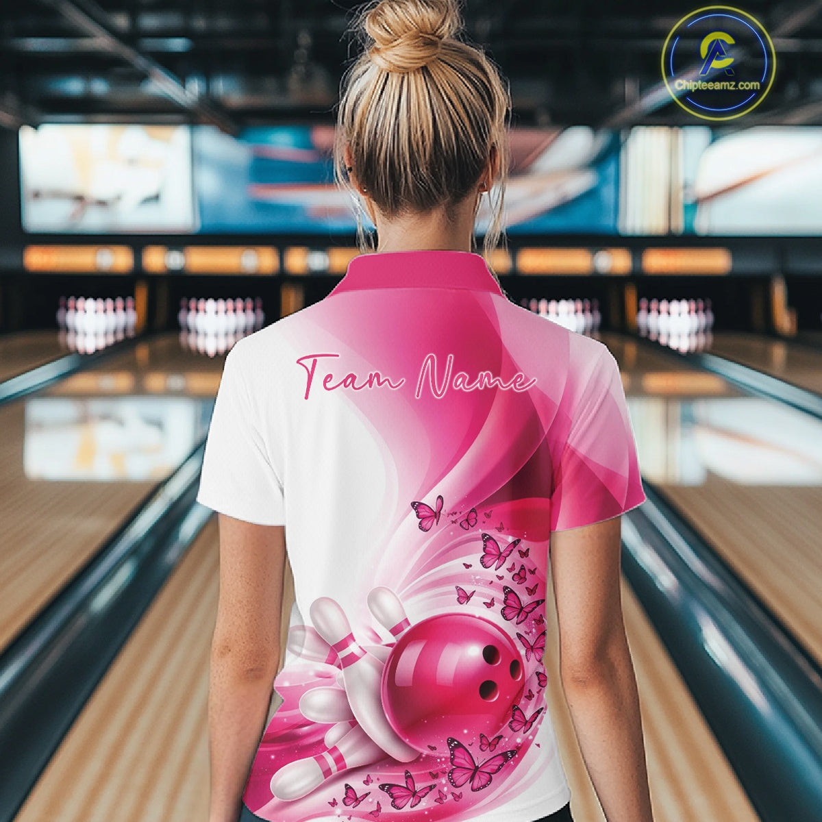 Back view of a white and pink women s bowling polo shirt showcasing butterfly artwork and bowling graphics at the bowling lane.