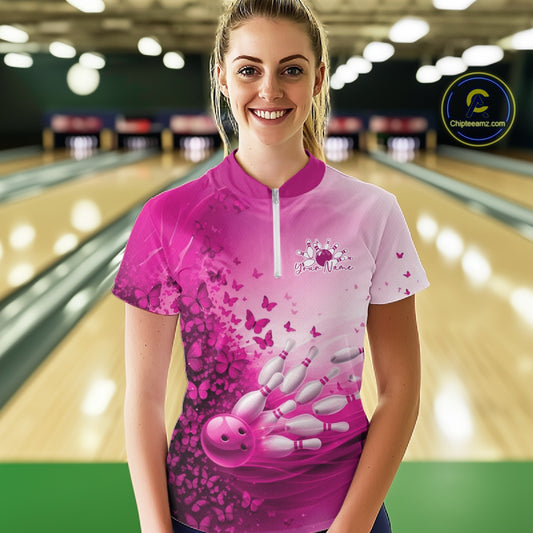 Woman wearing a pink bowling shirt with a design of a bowling ball and pins in a bowling alley.