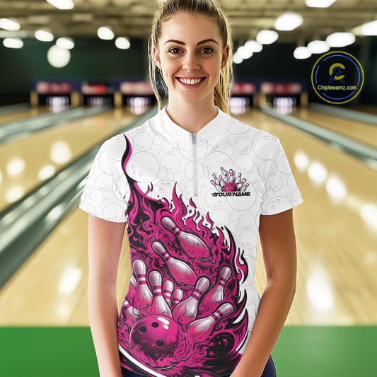Front view female model at bowling lane wearing white and pink quarter zip shirt showing flaming bowling ball crashing into pins with energetic fire illustration.