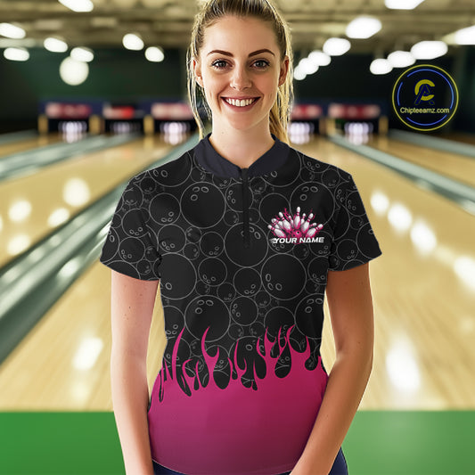 In a bowling lane, front view of a female model wearing a black quarter-zip shirt with vibrant pink flames and bowling ball pattern graphics creating a bold bowling action scene.