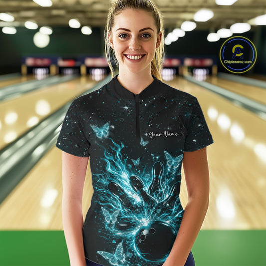 Female model wearing a black and turquoise blue bowling quarter-zip shirt at the lane with glowing butterflies and cosmic details.