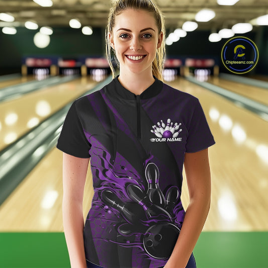 Female model in a bowling alley wearing a black and purple quarter zip shirt, front view featuring fiery bowling ball striking pins with geometric accents