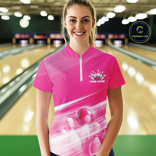 Front view of a female model at the bowling lane wearing a pink quarter zip shirt with bowling ball and pins geometric graphics.