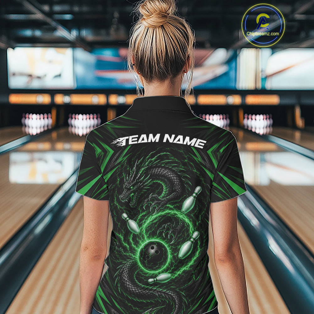 A woman viewed from behind wearing a black bowling-themed short-sleeve shirt with a green dragon and bowling ball graphic, and the text 'TEAM NAME' across the shoulders. The background shows a blurred bowling alley with lanes and pins.