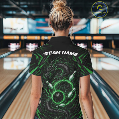 A woman viewed from behind wearing a black bowling-themed short-sleeve shirt with a green dragon and bowling ball graphic, and the text 'TEAM NAME' across the shoulders. The background shows a blurred bowling alley with lanes and pins.