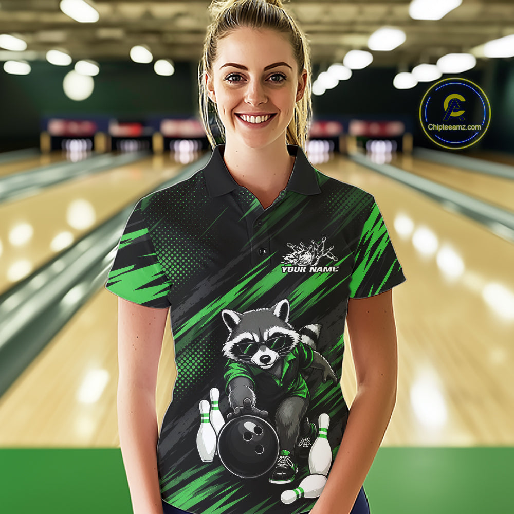 A woman stands in a bowling alley wearing a custom black and green short-sleeve polo shirt with a raccoon graphic holding a bowling ball and pins, and placeholder text on the chest. 