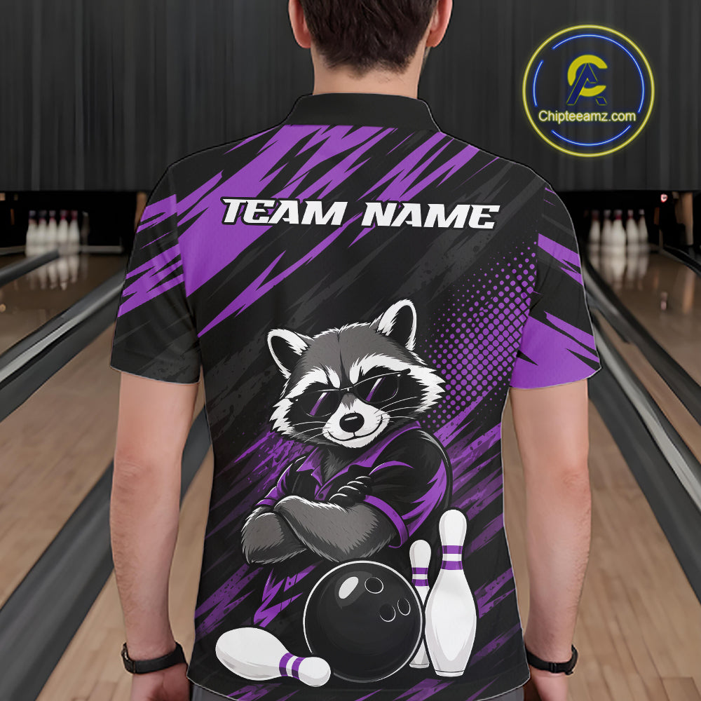 A person shown from the back wearing a short-sleeve polo bowling shirt in a bowling alley. The shirt is black with bold purple graphic stripes and a large raccoon illustration sitting on bowling pins, with the text 'TEAM NAME' across the upper back.