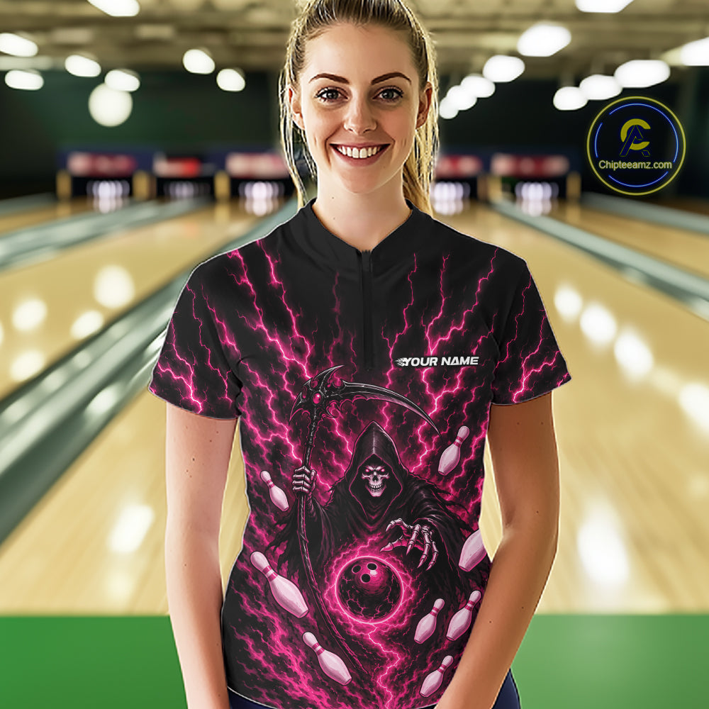 A woman wearing a black bowling-themed graphic quarter zip shirt with a grim reaper design and pink lightning, standing in front of a blurred bowling alley background. The shirt features a mock collar, short sleeves, and a 'YOUR NAME' customization placeholder on the chest.