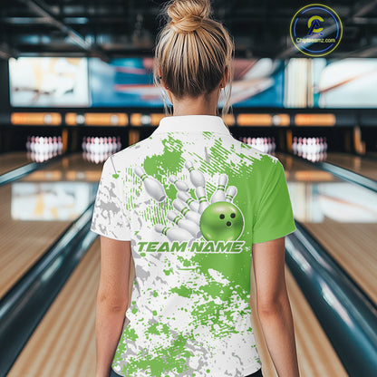 Back view female model at bowling lane wearing white polo with green and white splatter background, relaxed stance inside bowling center