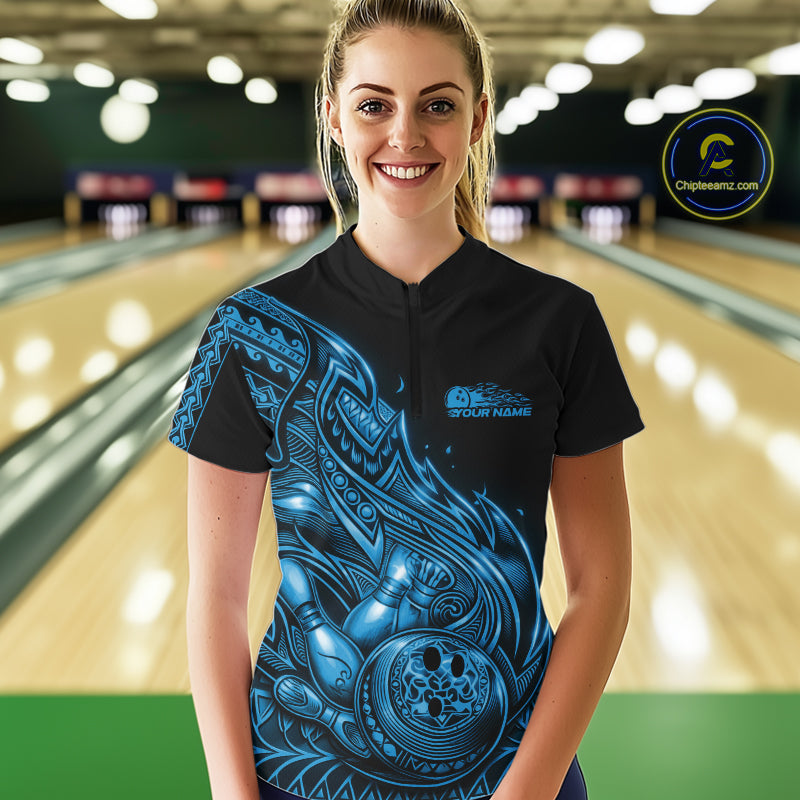 Female model wearing a black and blue bowling quarter-zip shirt at the lane with Polynesian-inspired flame bowling graphics.