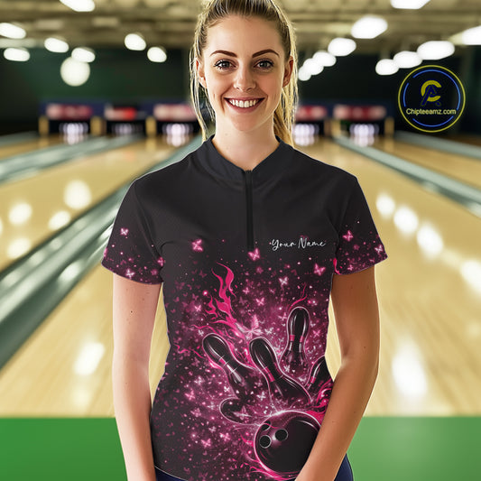 Female model wearing a black and pink bowling quarter-zip shirt at the lane with flaming bowling ball and butterfly graphics.