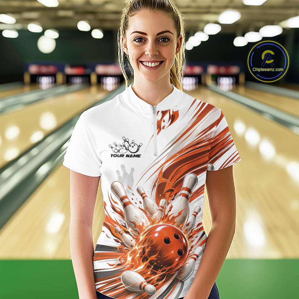A woman wearing a white short-sleeve bowling-themed shirt with a dynamic orange and white bowling ball graphic, standing in a bowling alley. The shirt features a white base with orange and white abstract streaks and a large bowling ball and pins design on the front.