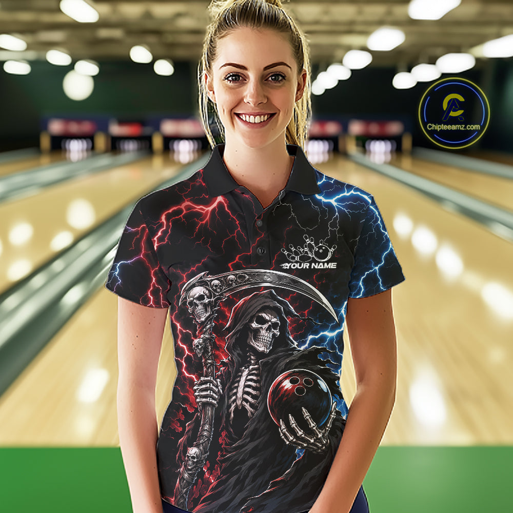 A woman wearing a black short-sleeve bowling shirt with a grim reaper graphic, red and blue lightning, and a bowling ball in the hand, standing in a bowling alley. 