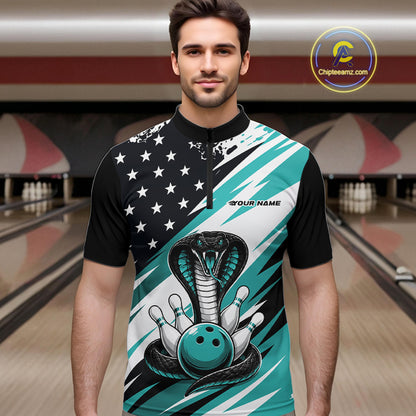 A man stands in a bowling alley wearing a black, white, and blue bowling shirt with stars, diagonal stripes, a cobra, pins, and an blue ball.