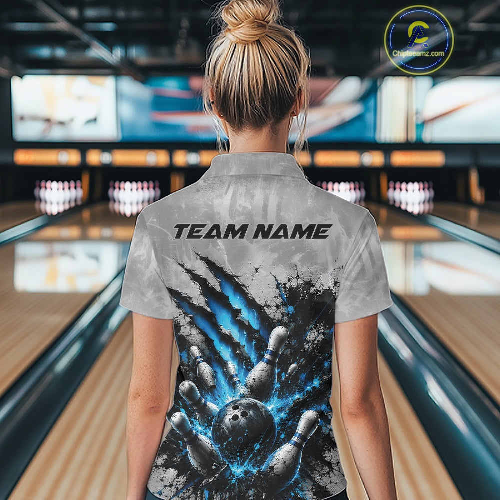 Back view of a female model wearing a gray bowling quarter zip shirt featuring a dramatic blue bowling ball striking pins graphic with claw-mark accents in a bowling lane.