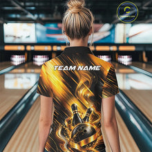 Load image into Gallery viewer, Back view of a female model wearing a bowling polo shirt showcasing a black and gold bowling ball hitting the pins graphic with flowing metallic ribbon accents in a bowling lane.