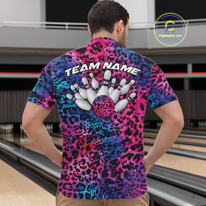 Back view of a man standing at a bowling alley, wearing a blue, purple, pink, and black leopard-print bowling polo with “Team Name” and bowling pins on the back.
