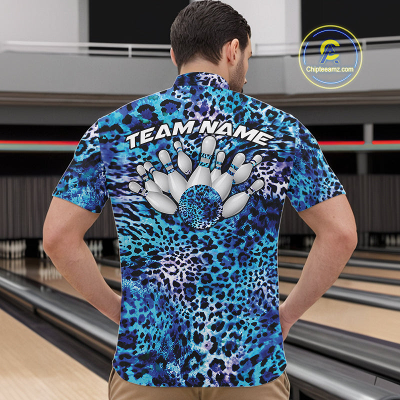 Back view of a man standing at a bowling alley, wearing a blue, teal, and black leopard-print bowling polo with “Team Name” and bowling pins on the back.
