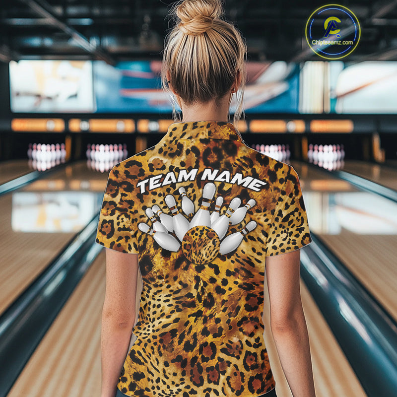 Back view of a woman standing at a bowling alley, wearing a gold, brown, and black leopard-print bowling polo with “Team Name” and bowling pins on the back.

