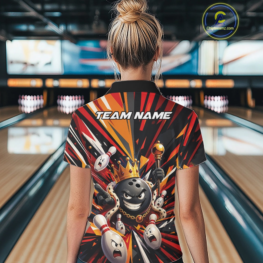 Back view of a female model at a bowling lane wearing a black, red, and orange bowling quarter-zip shirt featuring a crowned cartoon bowling ball holding a royal scepter alongside animated bowling pins with vibrant radiating color bursts.