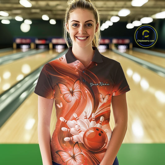 Female model at the bowling lane wearing an orange bowling polo with bowling strike artwork and butterfly details.