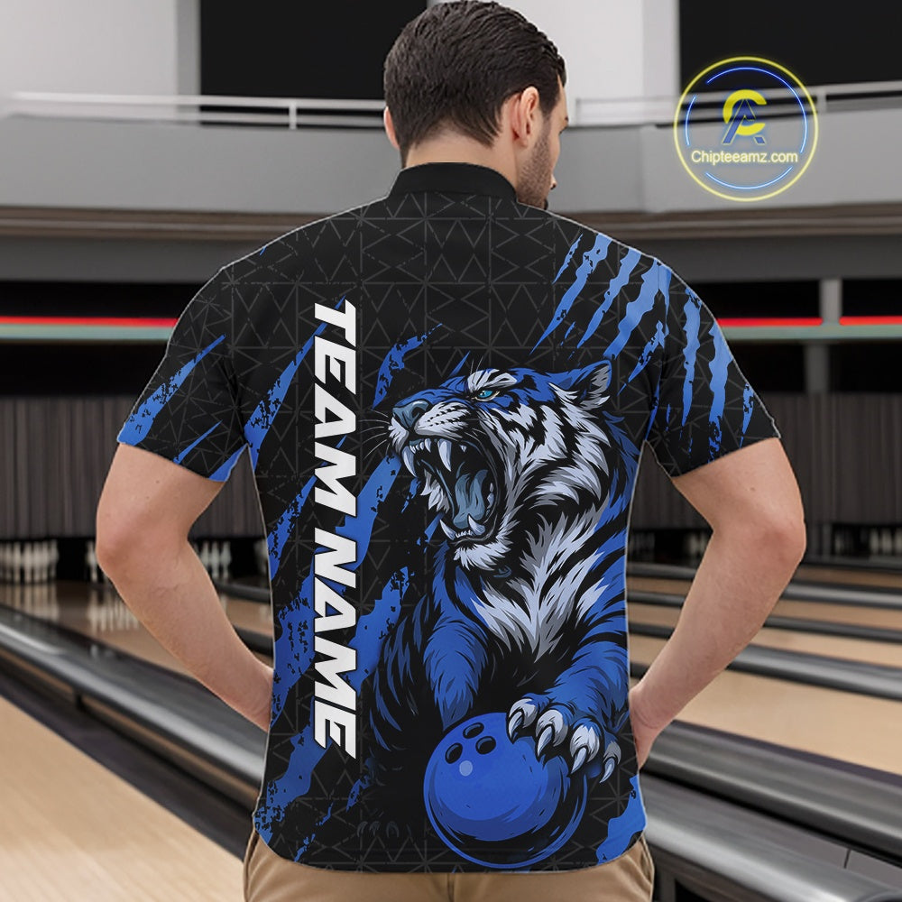 Front view of a male model at a bowling lane wearing a black and mid blue bowling quarter-zip shirt featuring a roaring tiger holding a mid blue bowling ball with coordinated claw-stripe graphics and a geometric background pattern.