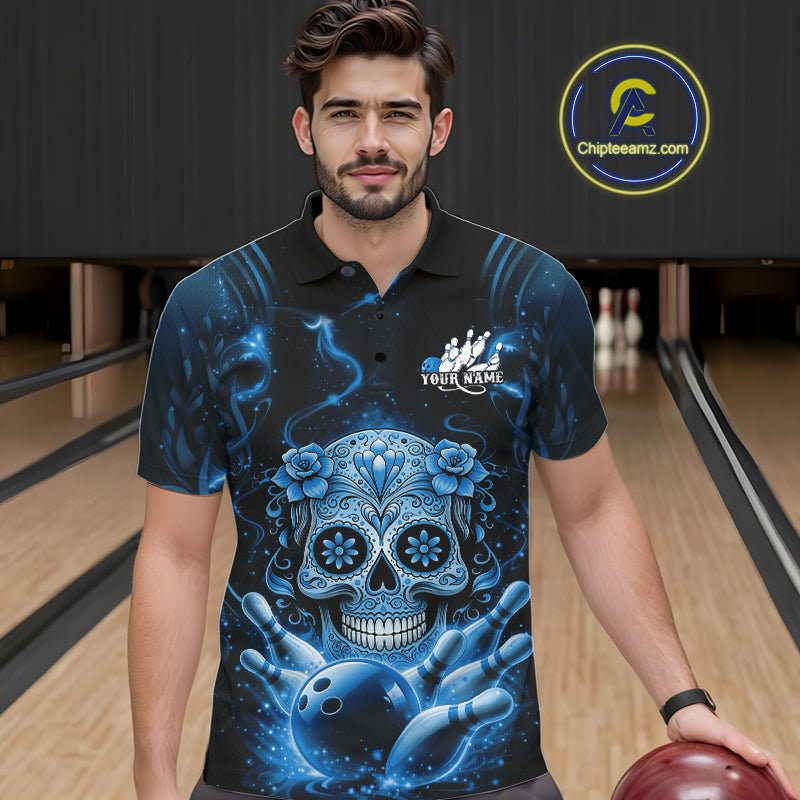Male model in a bowling lane wearing a black and blue polo shirt with floral sugar skull artwork above a bowling ball and scattered pins.