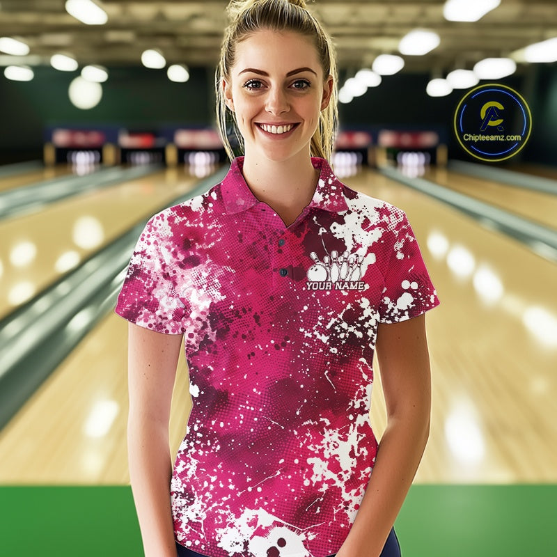 Woman wearing a pink and white patterned bowling shirt with a logo and text in a bowling alley.
