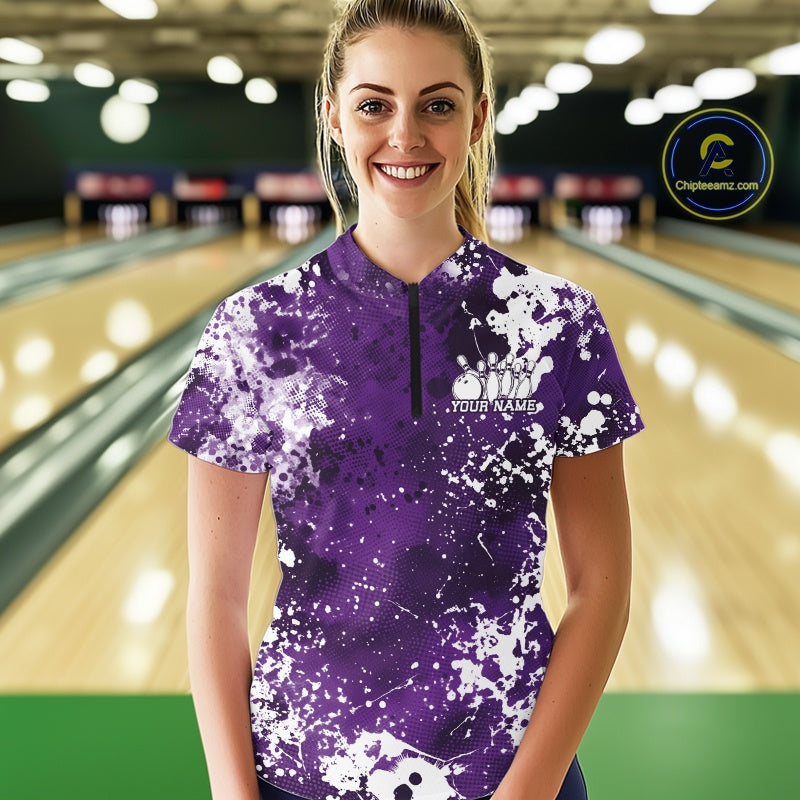 Woman wearing a purple and white bowling shirt with splatter design in a bowling alley.