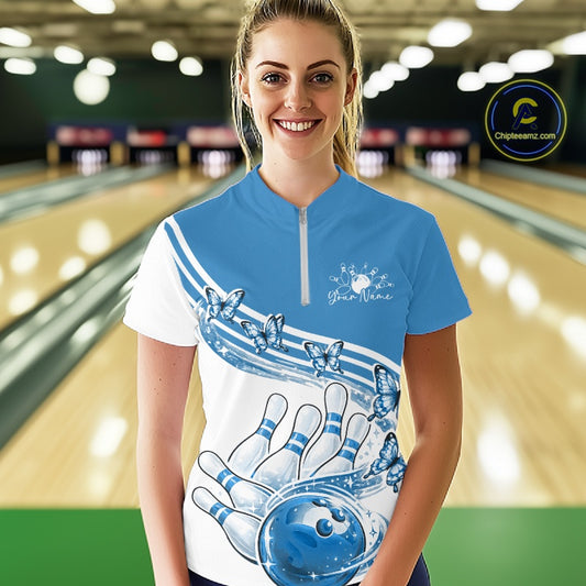Female model wearing a white and blue bowling quarter zip with butterfly artwork and bowling graphics, front view inside a bowling alley