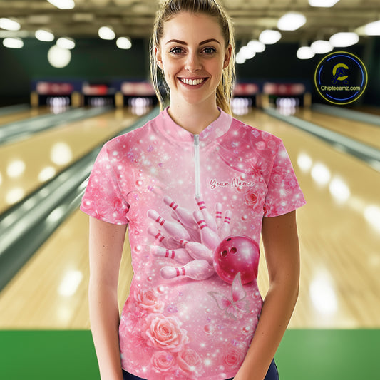 Female model at a bowling lane wearing a pink quarter zip bowling shirt with butterfly and sparkling diamond themed bowling artwork.