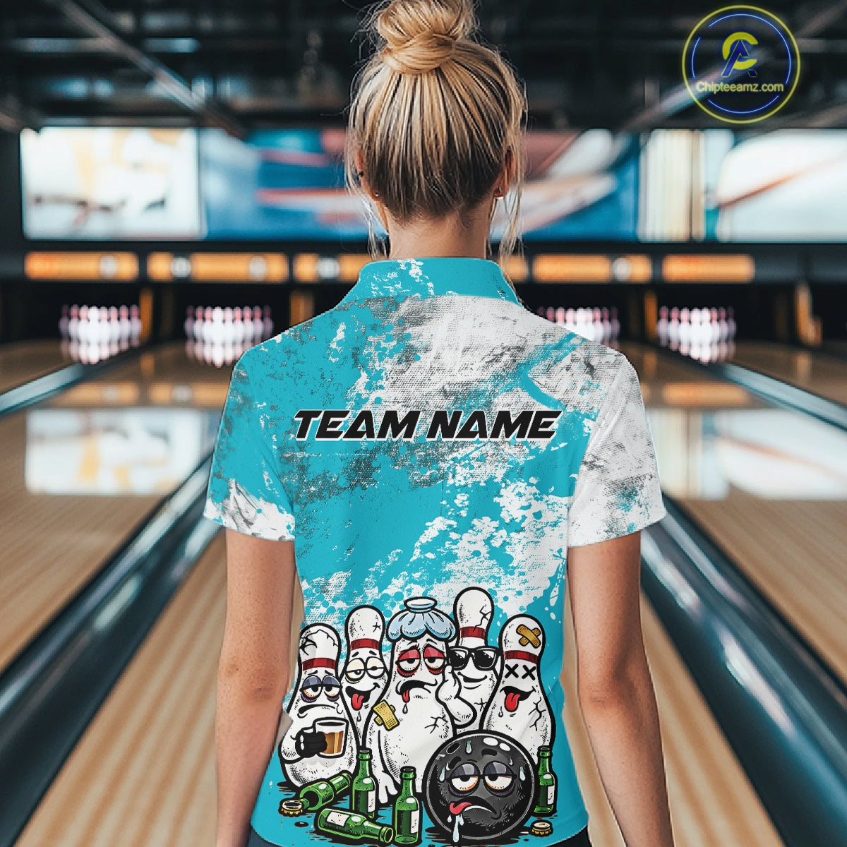 Back view of a female model in a bowling lane wearing a bowling quarter-zip shirt with turquoise blue and white grunge splatter design, featuring cartoon bowling pins and beer bottle graphics around a bowling ball.