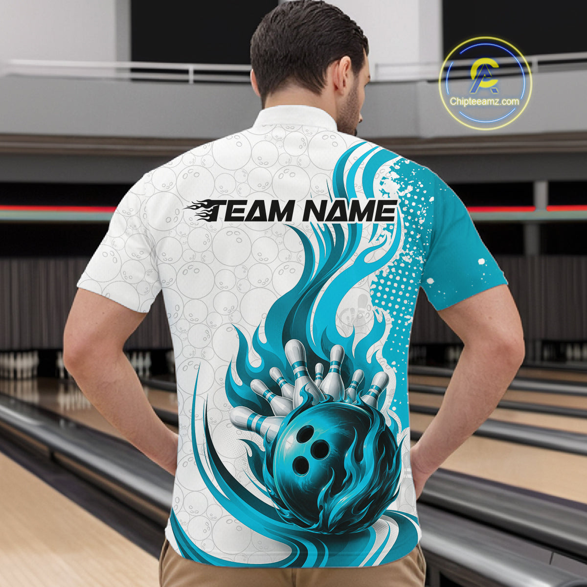 A man viewed from behind wearing a short-sleeve bowling-themed shirt in a bowling alley. The back of the shirt is white with a large teal and blue graphic of a bowling ball and flames, plus the text 'TEAM NAME'.