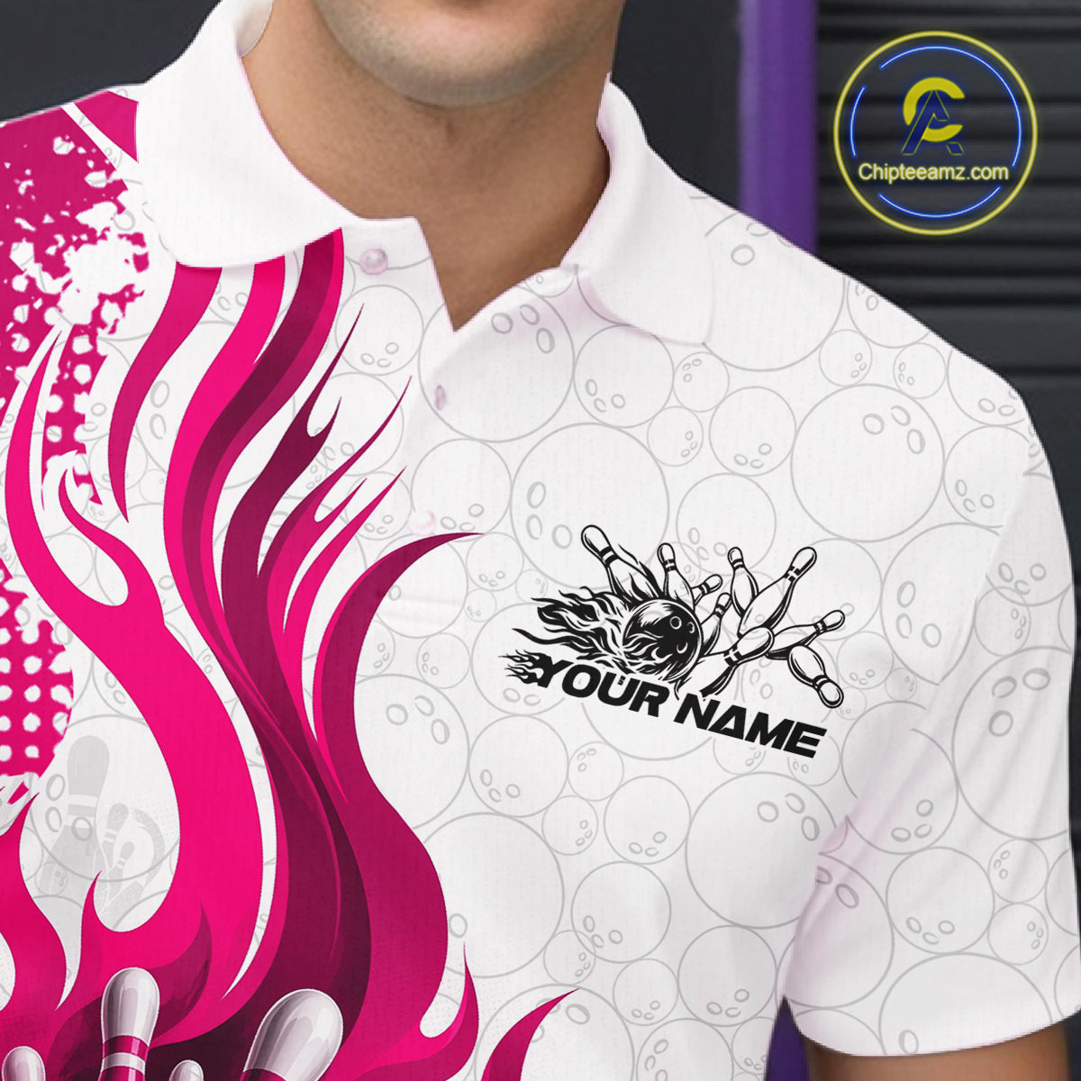 A close-up of a white short-sleeve polo shirt with a black bowling pin graphic and the text 'YOUR NAME' on the chest, featuring a bright pink flame design on the left side and a subtle gray bowling ball pattern across the background.