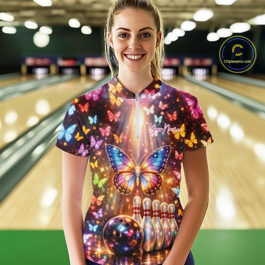 Female model at a bowling lane wearing a quarter-zip bowling shirt with colorful butterflies, bowling pins, a bowling ball, and sparkling light accents.