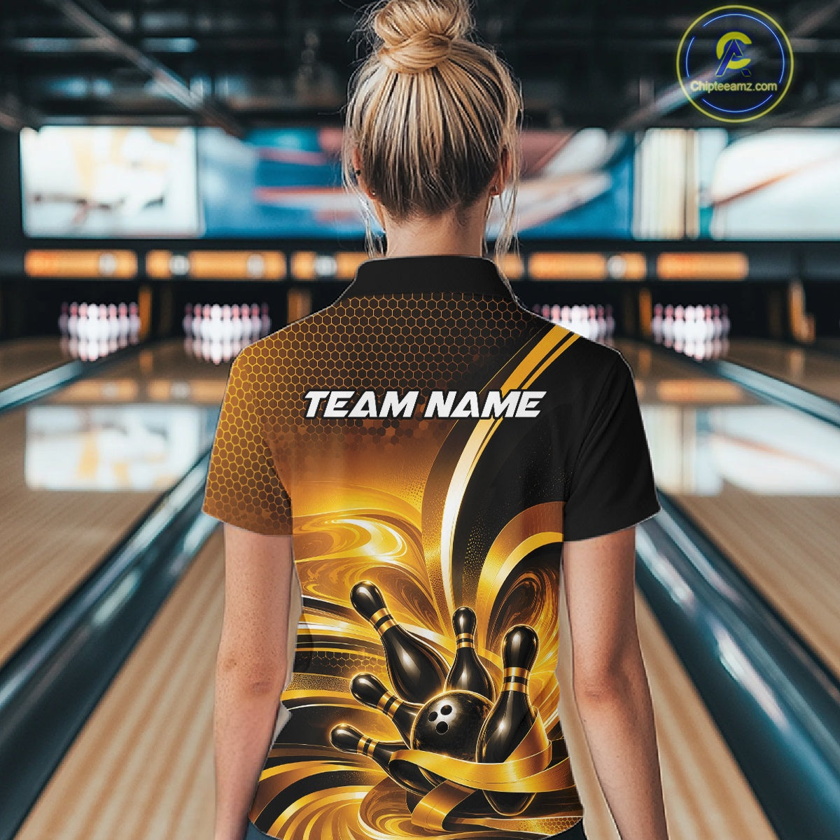 Back view of a female model wearing a bowling quarter zip shirt with glossy gold and black bowling ball and pins artwork in a bowling lane.